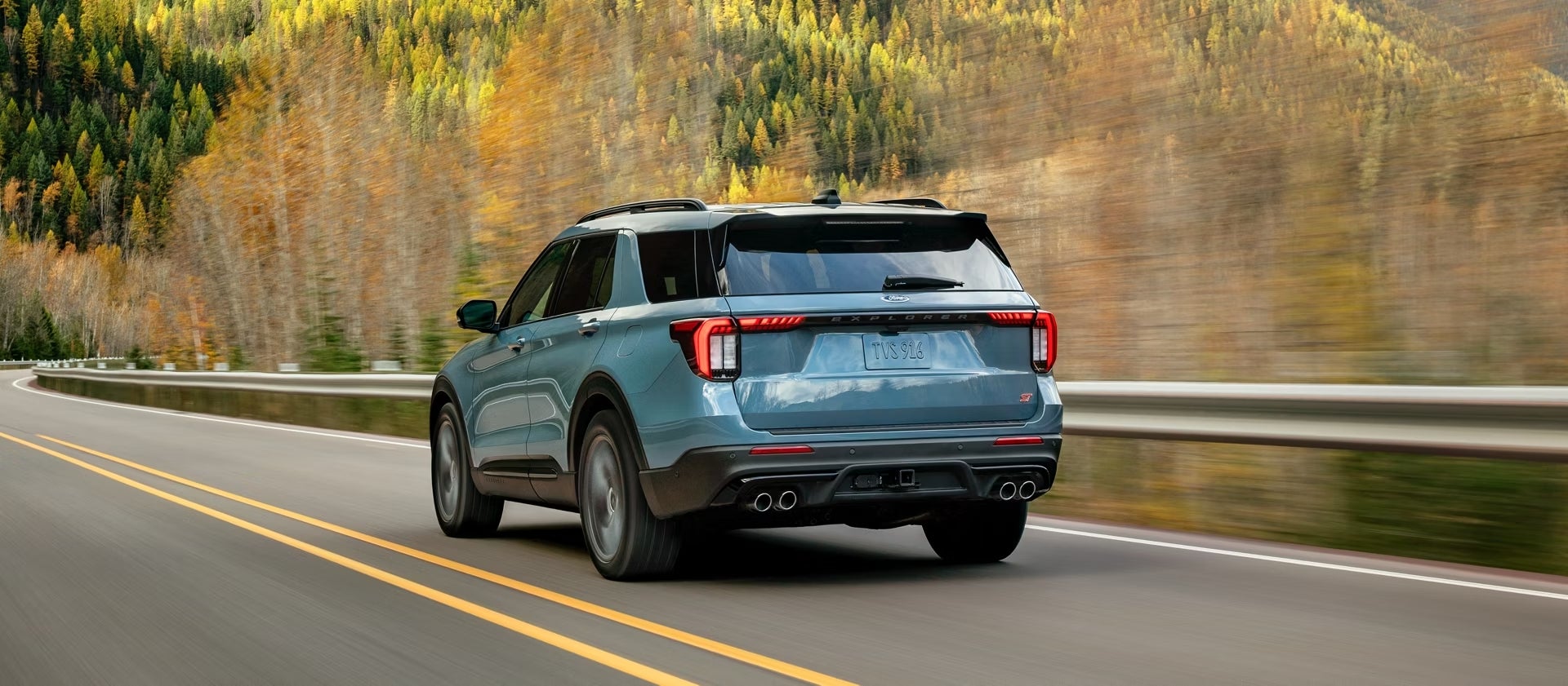 The new 2026 Ford Explorer in Chandler AZ drives away from the viewer to the left on a rural two-lane road surrounded by trees.