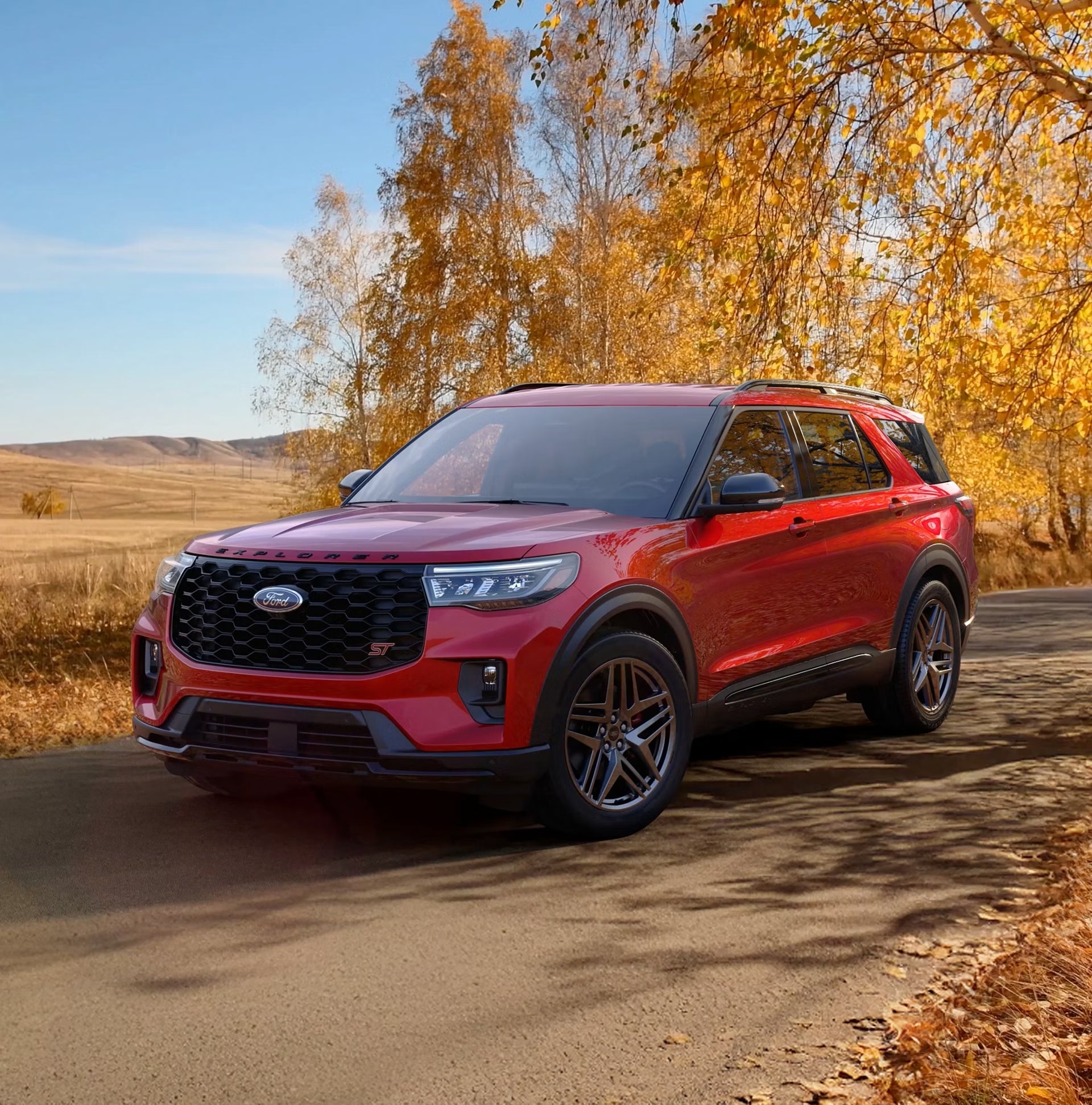 A red new Ford Explorer in Chandler AZ drives towards the viewer to the left on a dirt road with yellow grassy plains in the background.