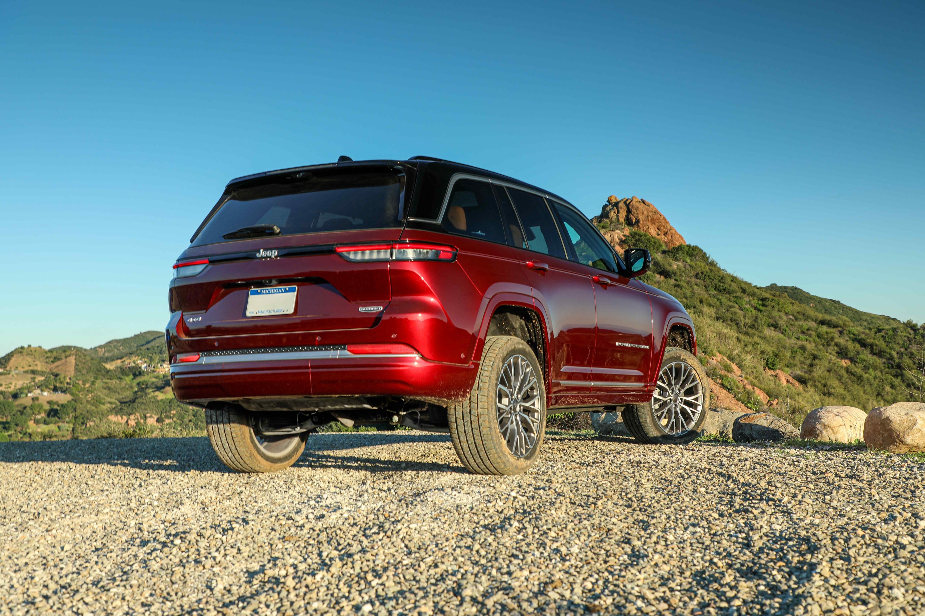 A red 2026 Jeep Grand Cherokee in Chandler AZ drives away from the viewer to the right up a rocky mountain trail.