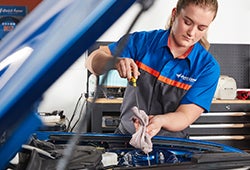 A professional Earnhardt Ford technician conducts an oil change on a blue car with Ford Warranty in Chandler AZ.