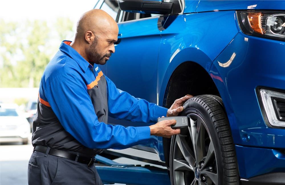 A professional Earnhardt Ford technician checks the tire pressure on a blue car with Ford Warranty in Chandler, AZ.